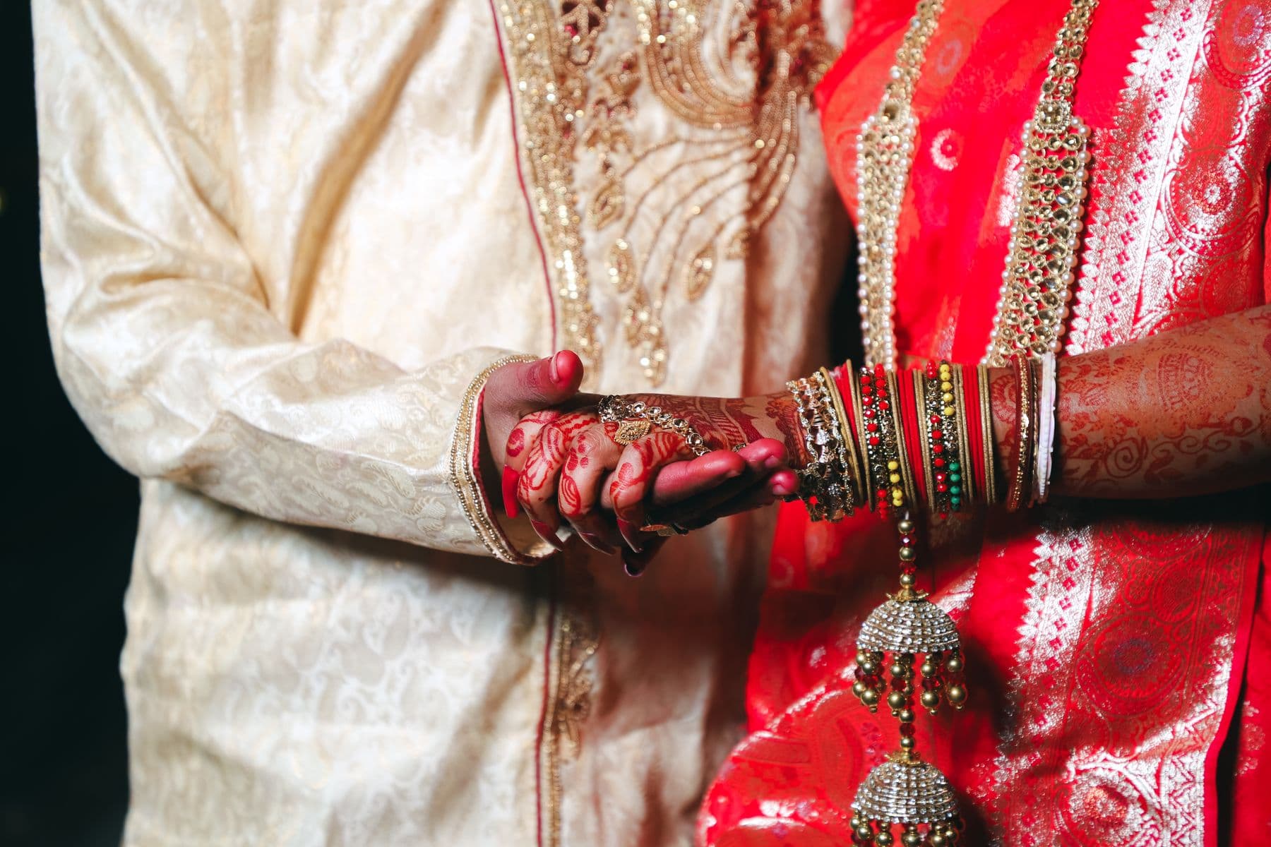 A couple's hands and bangles in warm rose light — faces never shown